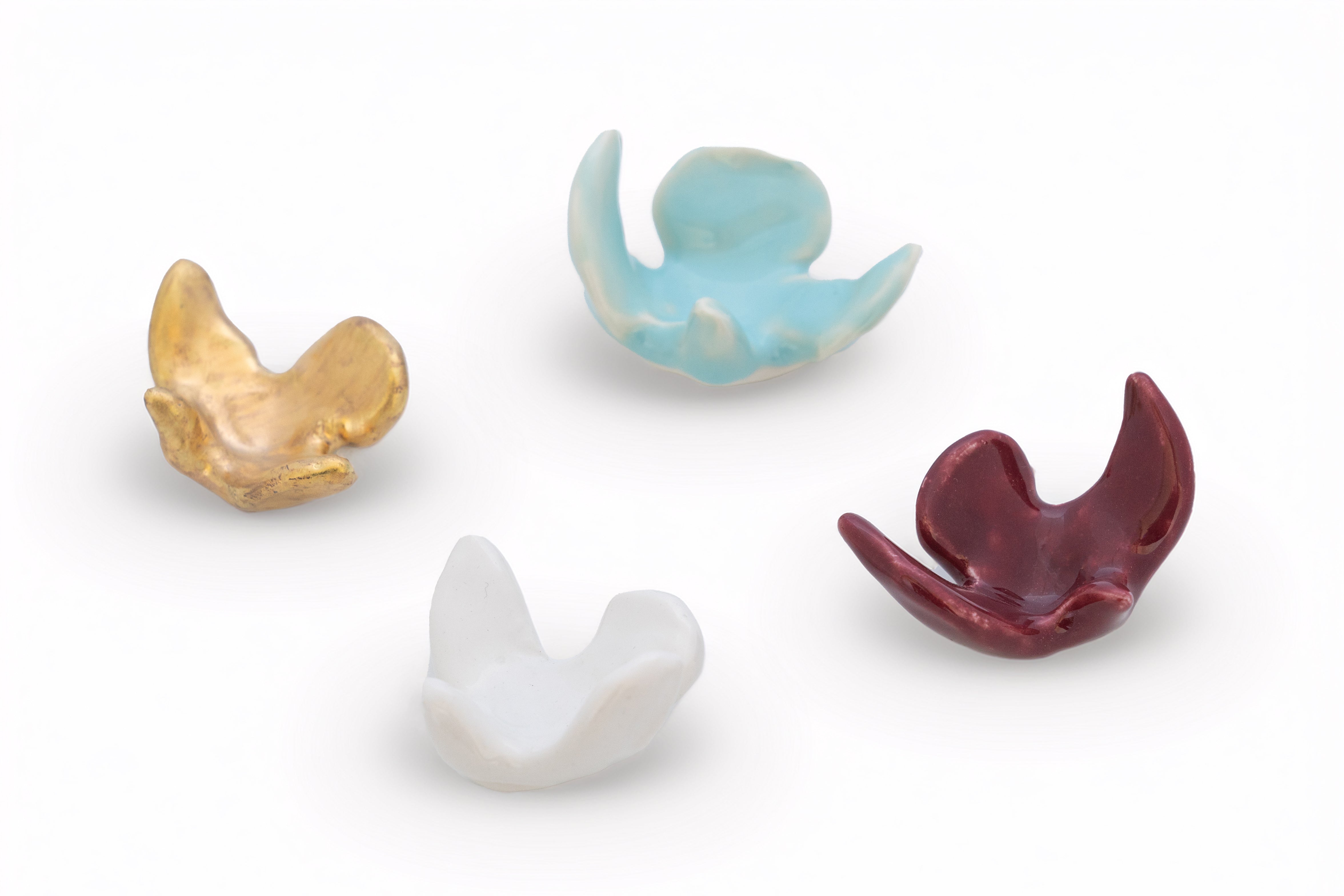 Four ceramic or porcelain bird figurines in gold, blue, white, and red glaze on a white background