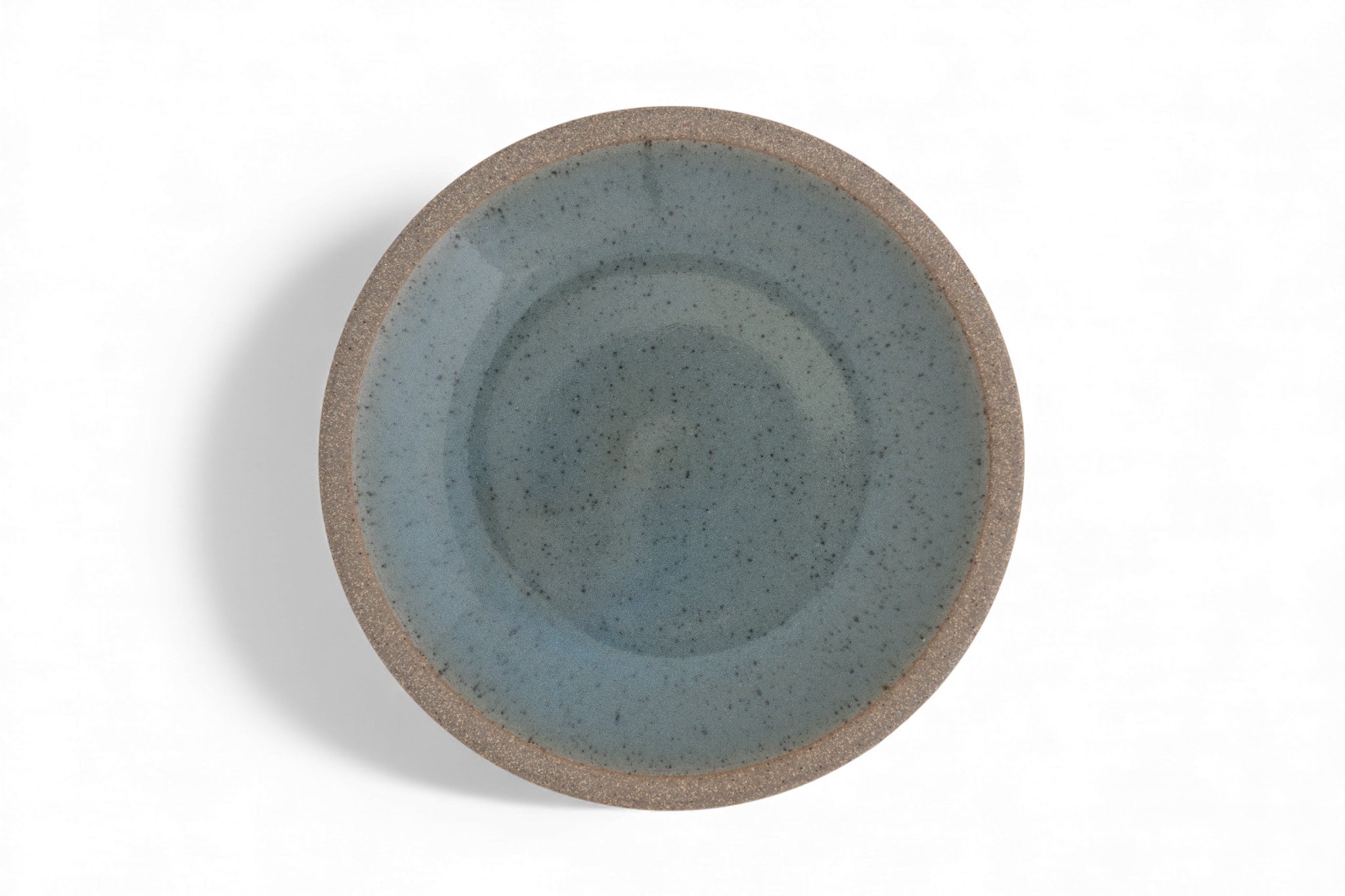 A stoneware dinner plate with a matte raw clay surface and interior glazed in shades of deep celadon green.
