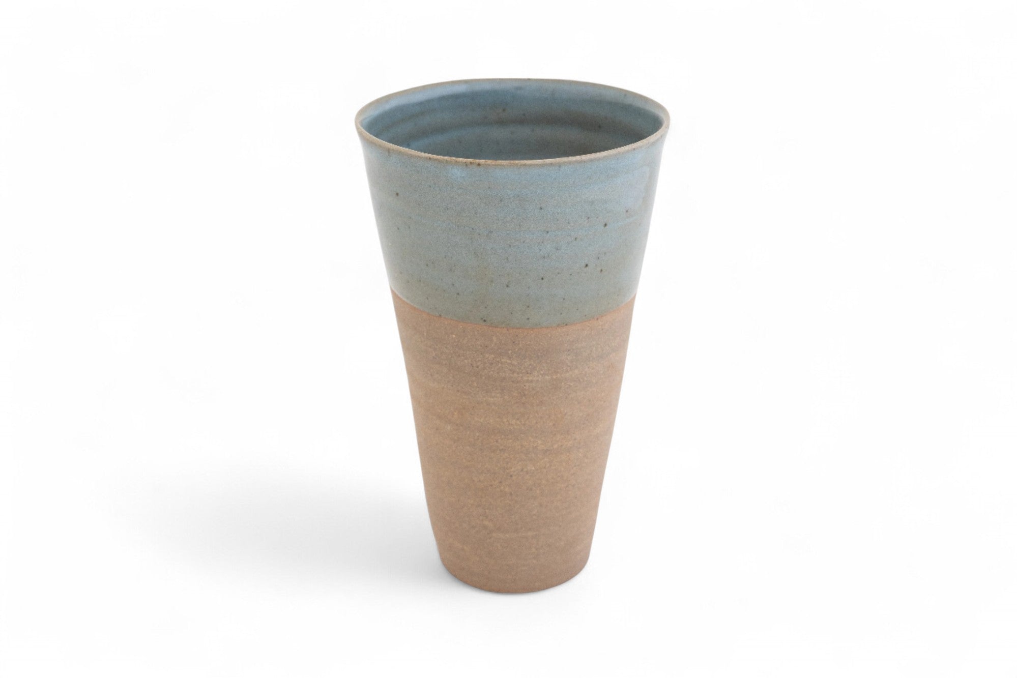 A hand-thrown stoneware beaker with a matte raw clay surface and a dipped, glazed edge in shades of deep celadon green.