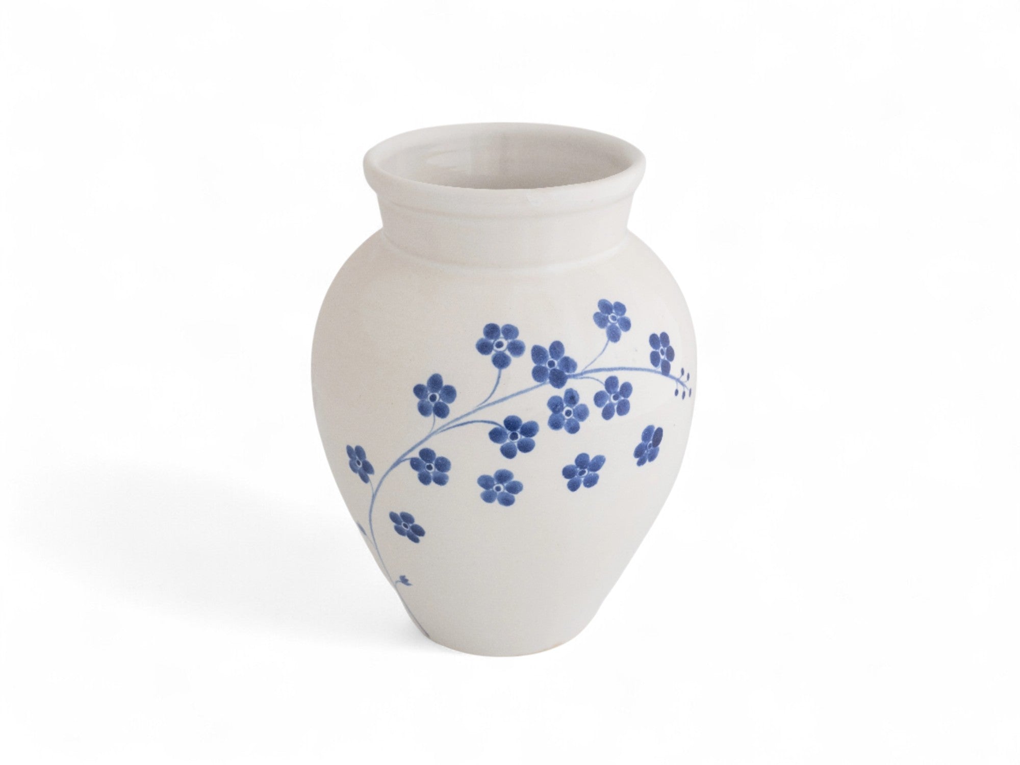 A hand-thrown, hand-dipped ceramic vase with a white glaze and blue floral patterns.