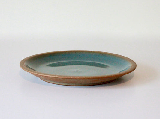 Raw clay plate with blue-green celadon glaze on inside surface