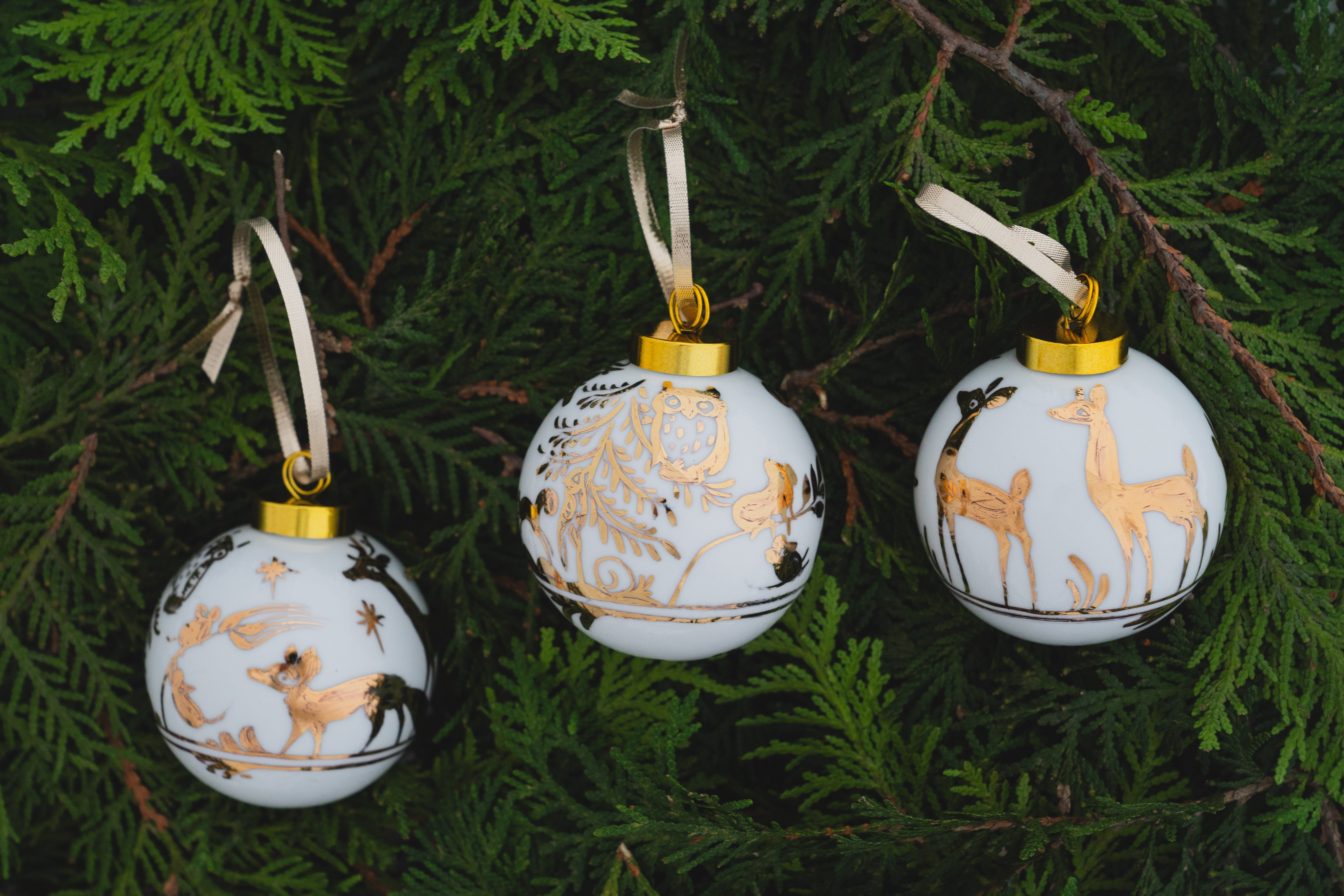 Three Christmas ornaments with deer designs on a green leaf background