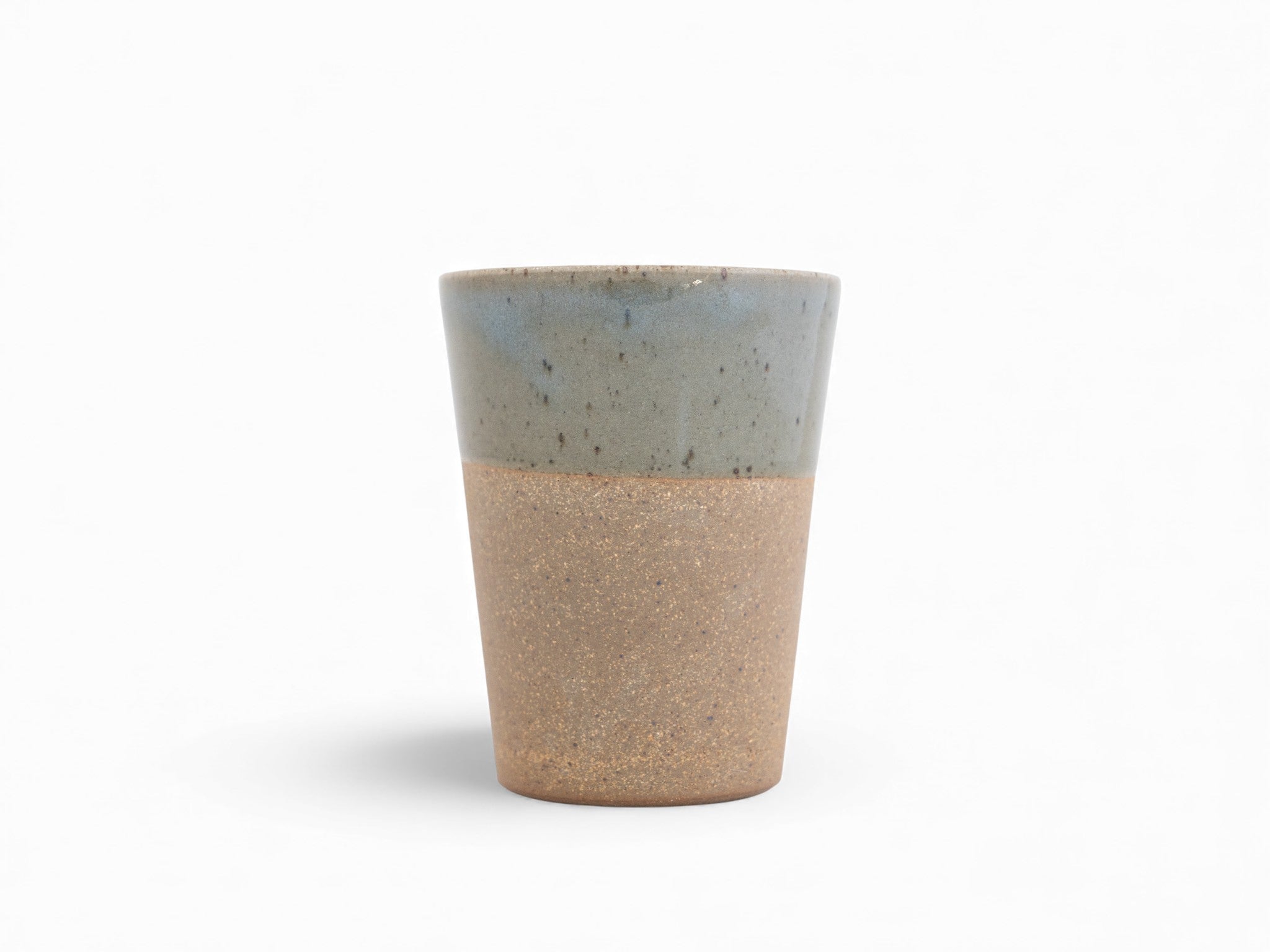 A stoneware beaker with a two-tone color scheme, featuring a matte raw clay surface on the exterior and a glossy glazed deep celadon green interior.
