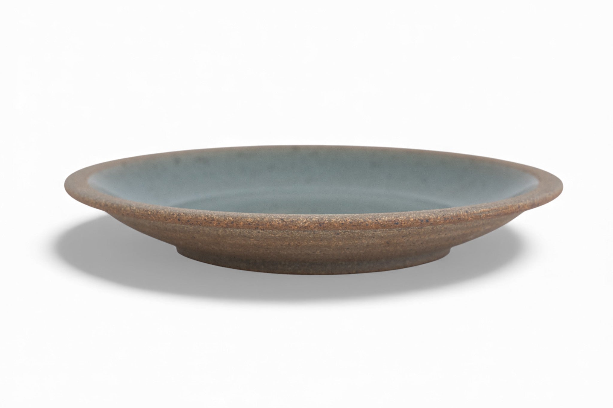 A stoneware dinner plate with a matte raw clay surface and interior glazed in shades of deep celadon green.