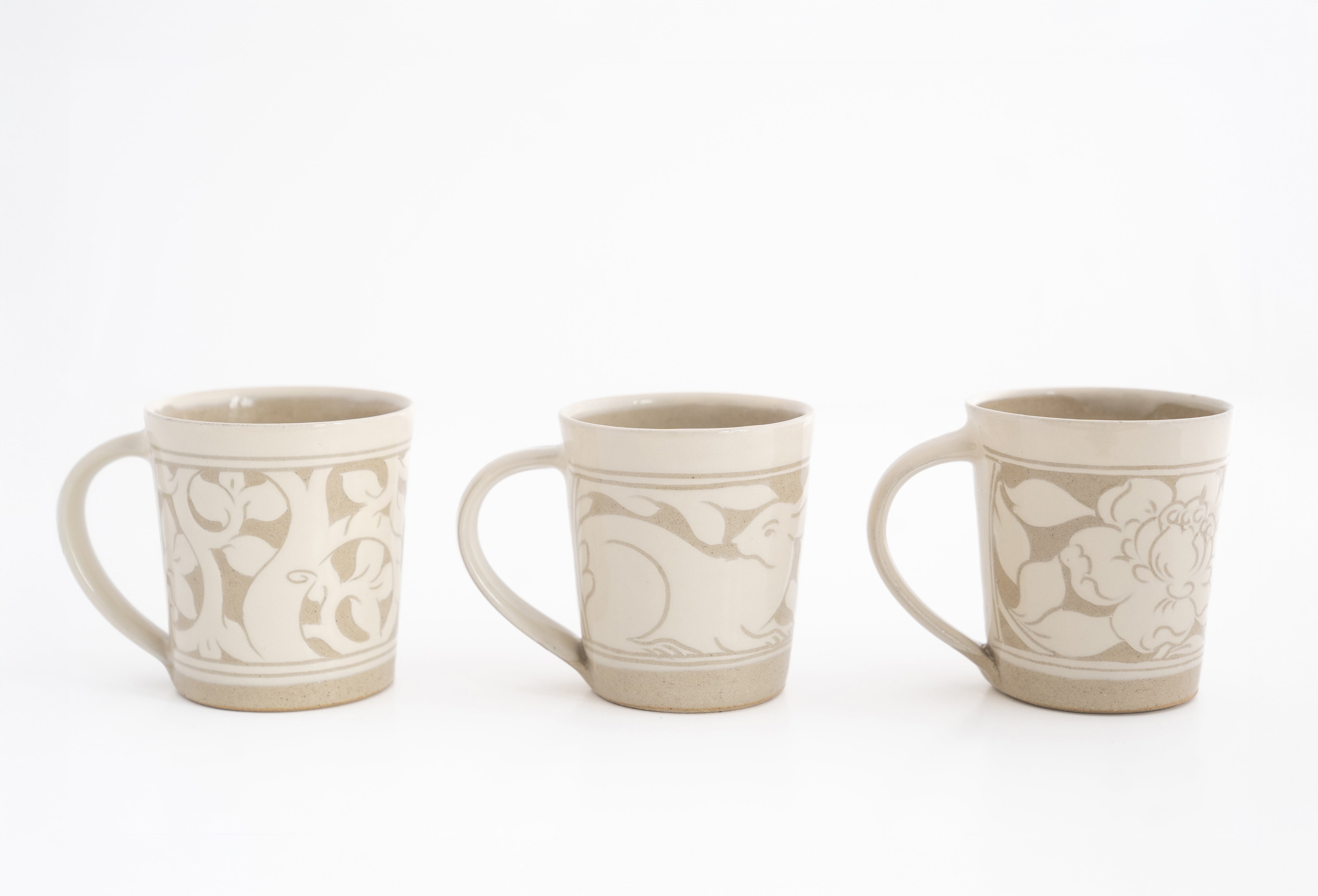 A set of three beige ceramic mugs with carved floral patterns, displayed against a white background.