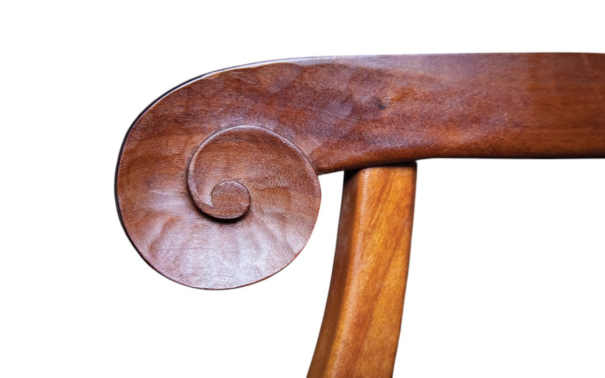 Close-up of a wooden chair arm with intricate scrollwork on a white background