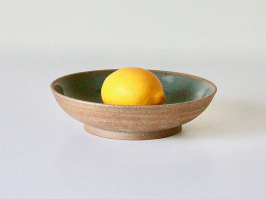 Raw clay pasta plate with blue-green celadon glaze on inside surface with a lemon